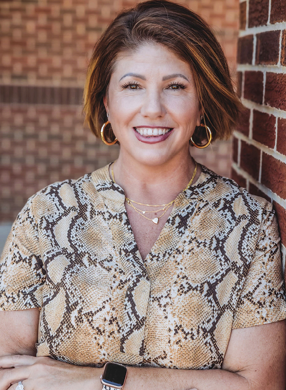 Woman with brown hair smiling and posing against brick wall